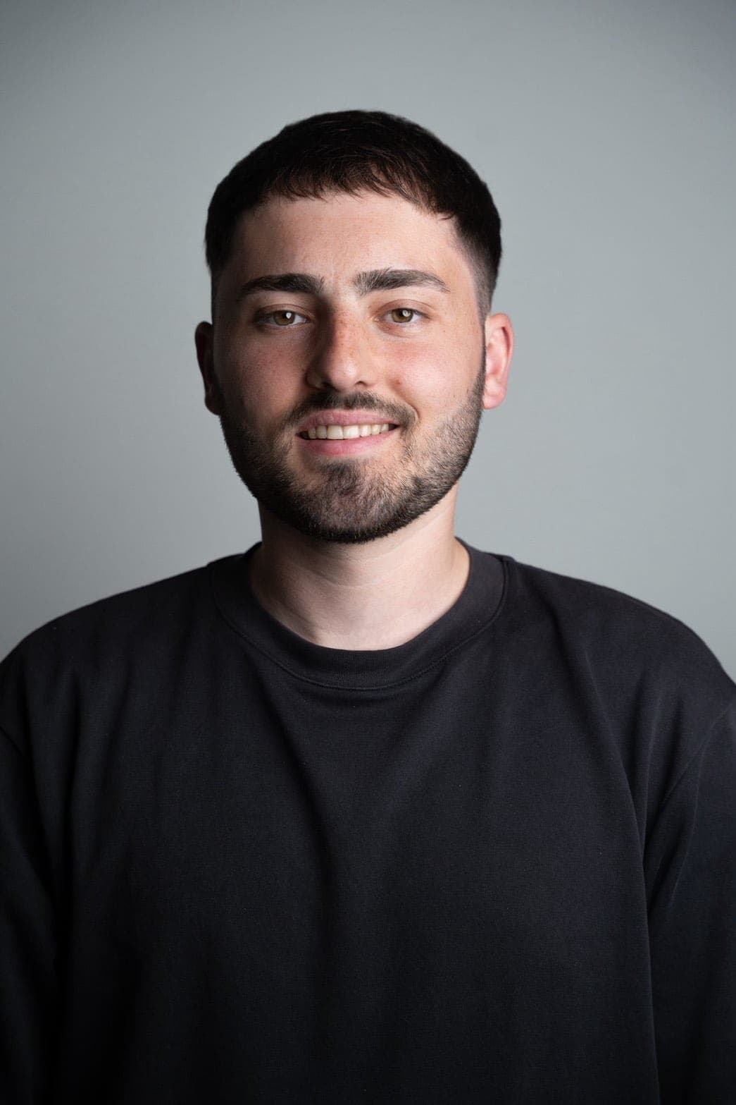 Portrait of Jannis, Tokyo-based photographer, smiling in a black sweater against a gray background
